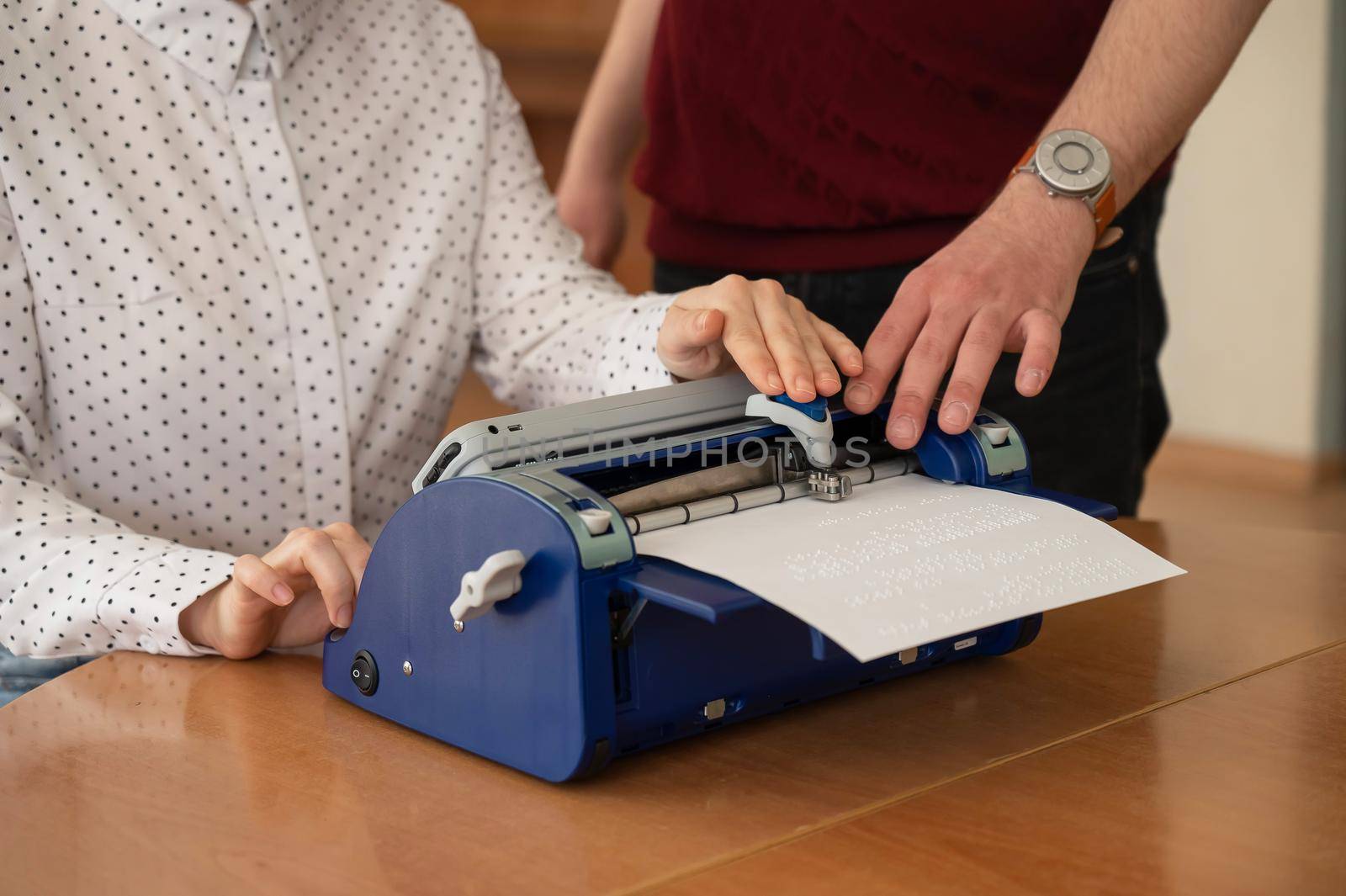 A man teaches a blind woman to type on braille machine