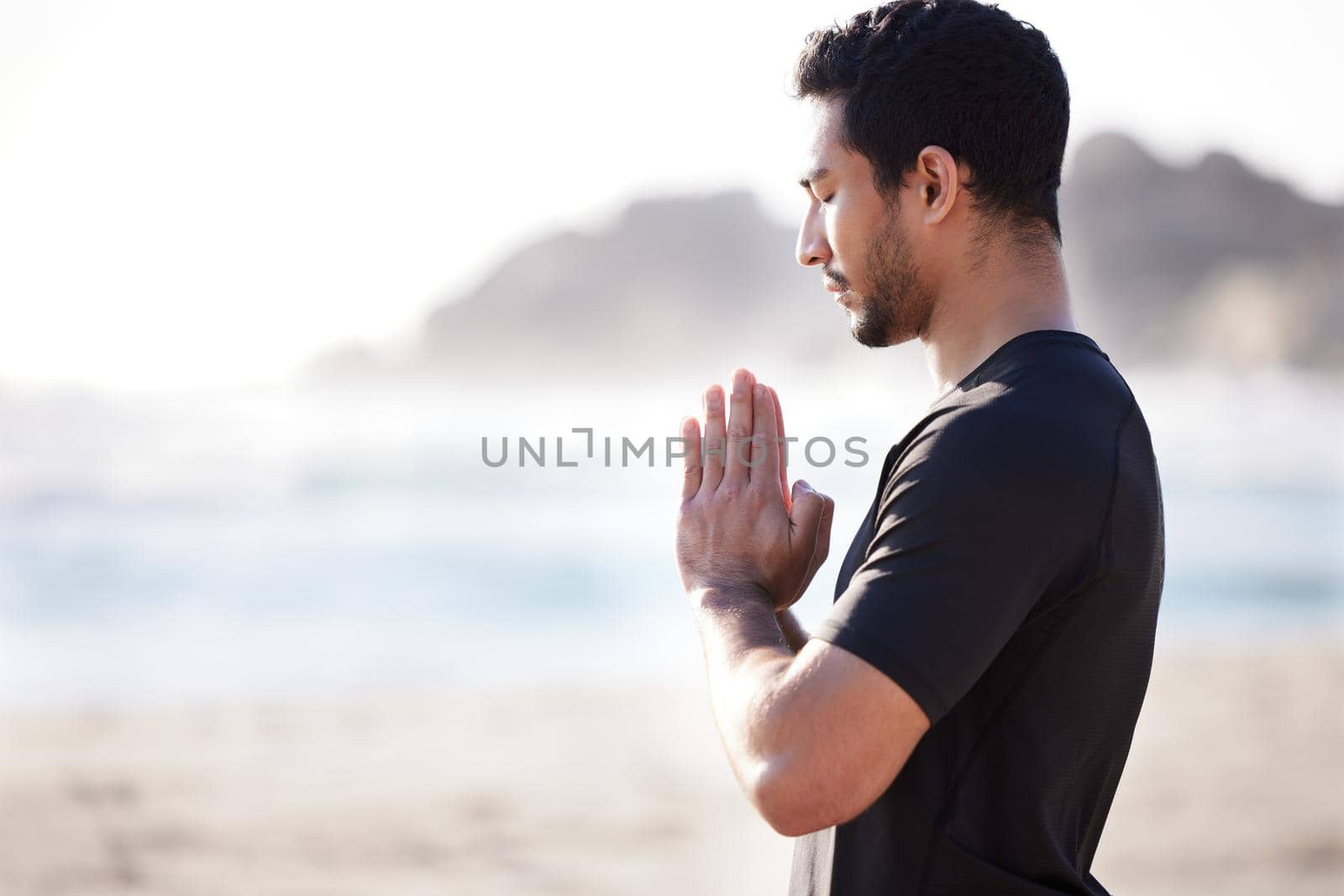 Cropped shot of a handsome young male athlete meditating on the beach.