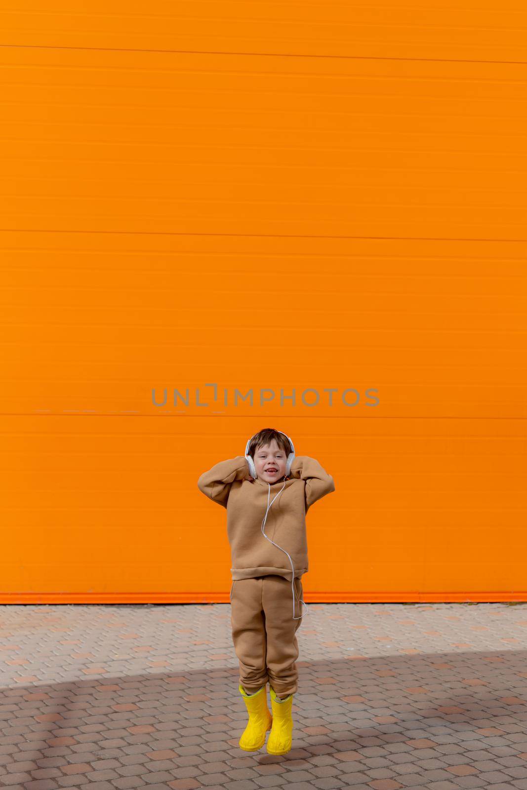 A boy listens to music with headphones on the background of an orange wall . Copy space. Mockup. An article about modern children. An article about modern music. Article about the choice of headphones. Urban lifestyle