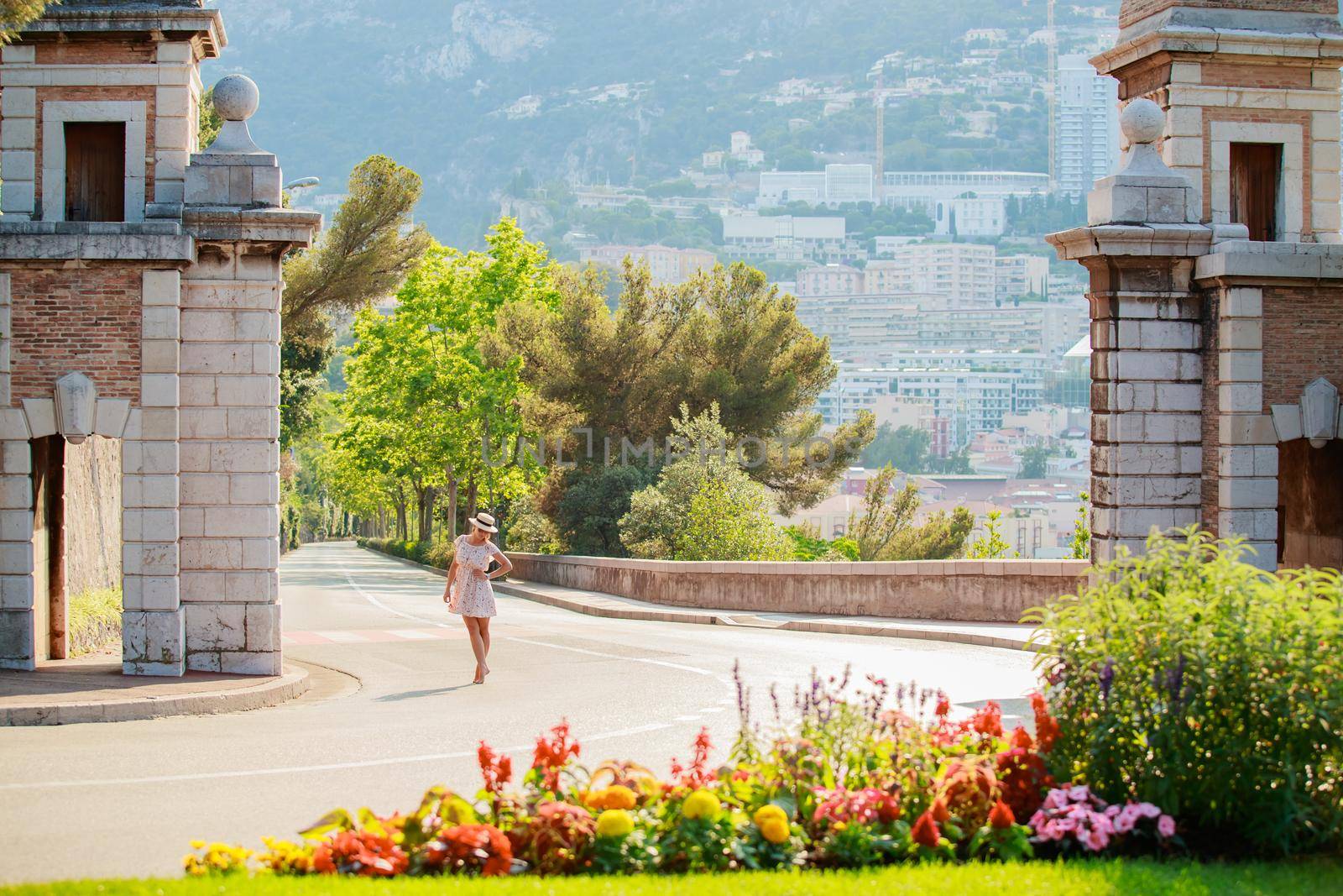 a bright beautiful girl in a light dress and hat walks along the streets of Monaco in sunny weather in the summer, luxury apartments of Monte Carlo on background. High quality photo