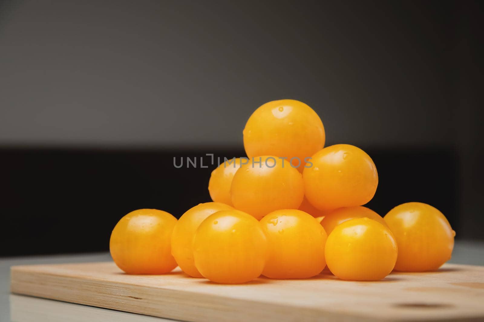 A heap of yellow cherry tomatoes on a wooden cutting board in the kitchen on a white table.