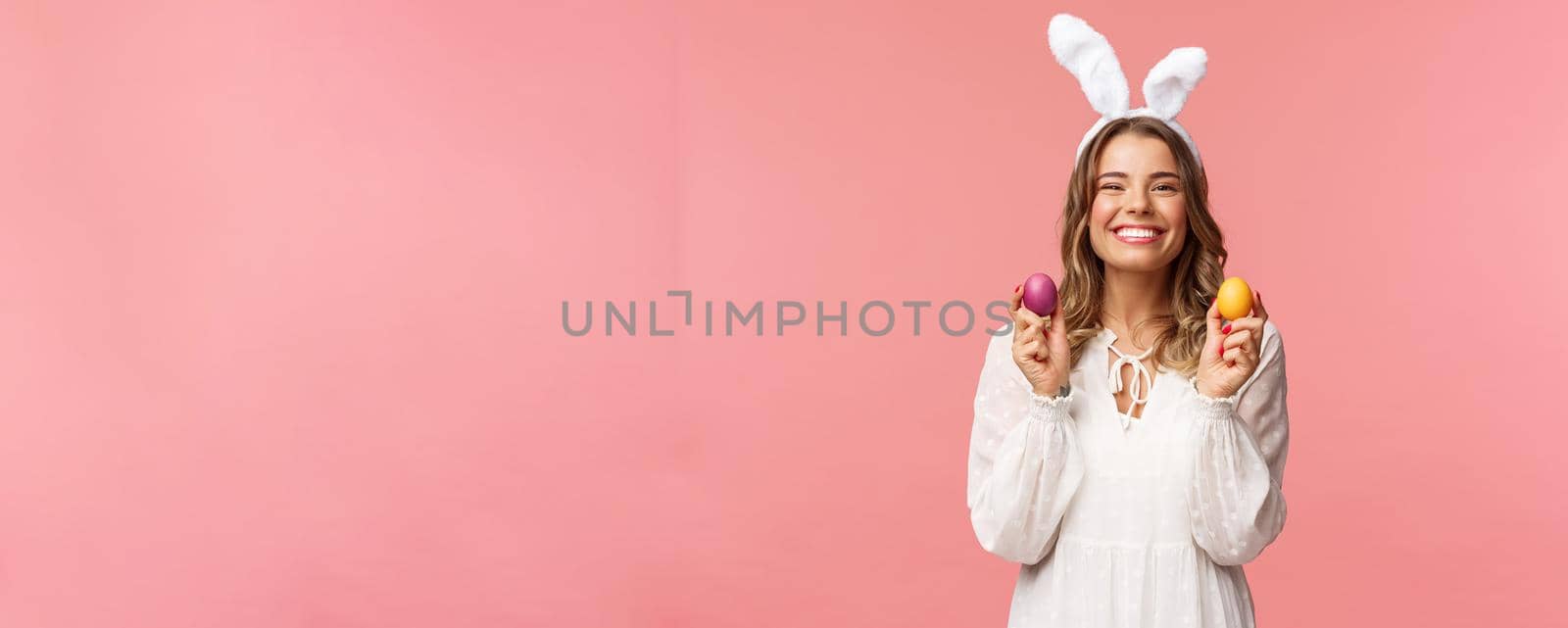 Holidays, spring and party concept. Portrait of lovely, cheerful blond girl in rabbit ears, holding colored eggs, celebrating Easter with family, enjoying spend traditional day with close people.