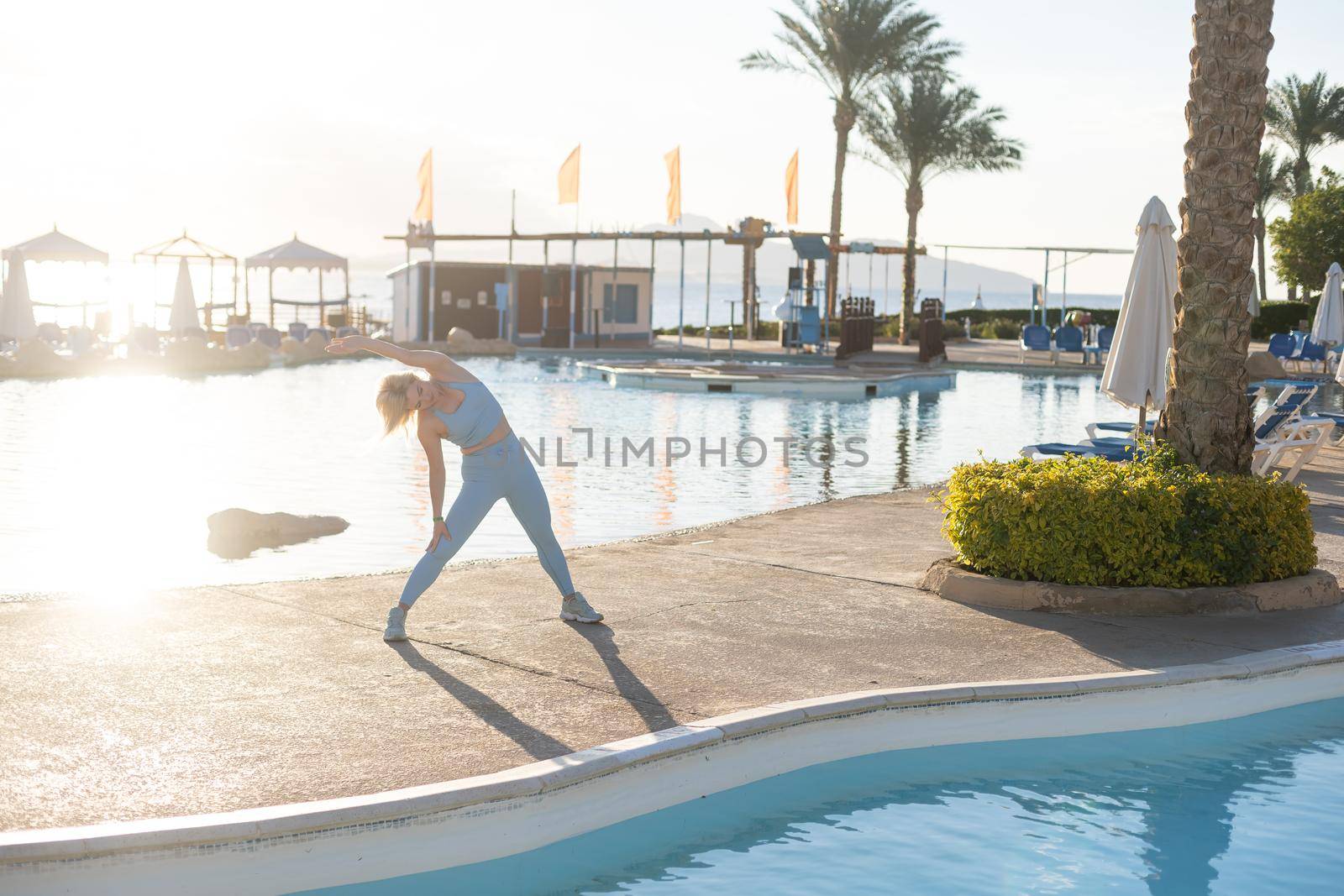 Young woman doing exercise to burn fat, keep fit. Sunset beach, blue sky background. Healthy lifestyle at training camp, outdoor fitness activity, family summer holiday