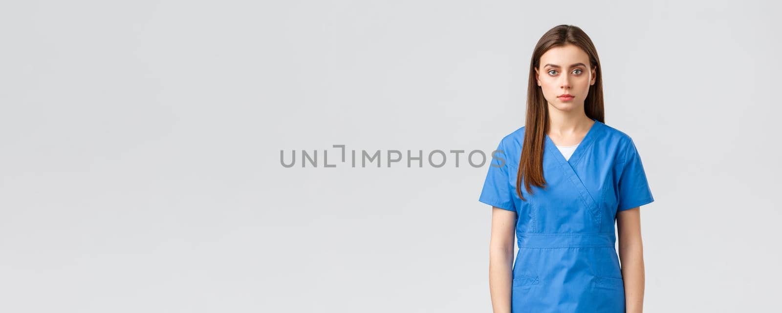 Healthcare workers, prevent virus, insurance and medicine concept. Serious-looking young medical worker, nurse or doctor in blue scrubs, looking determined and confident camera.