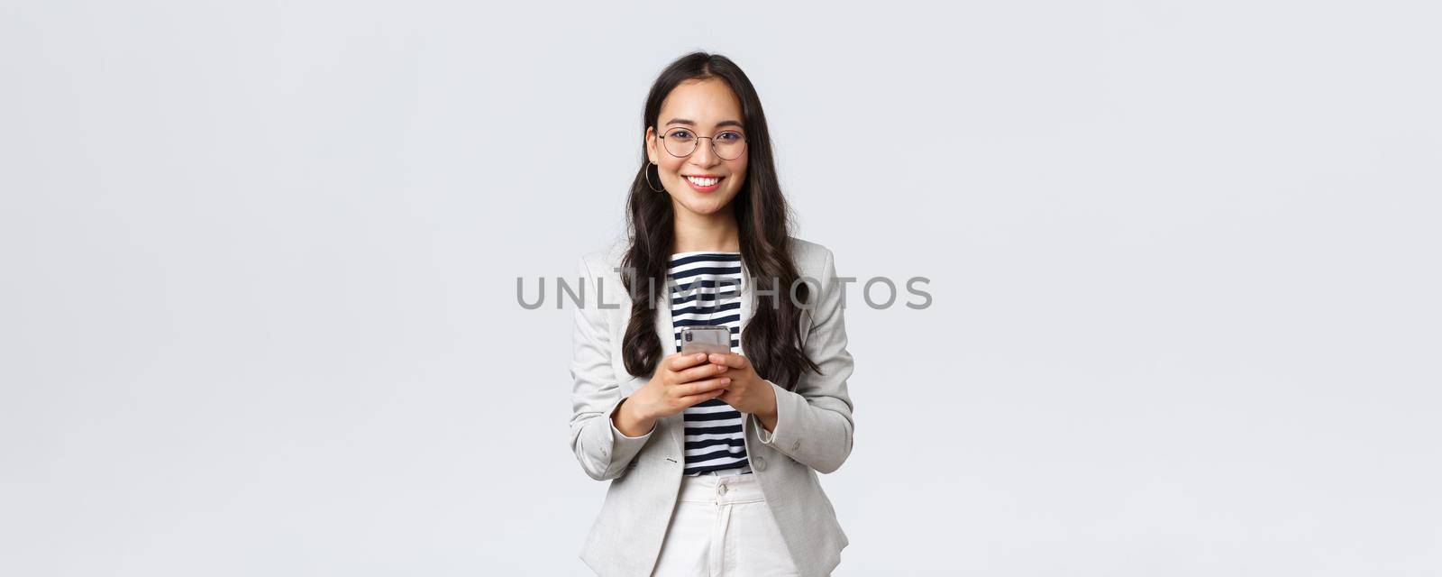 Business, finance and employment, female successful entrepreneurs concept. Smiling pleasant asian businesswoman, real estate broker wear glasses, using mobile phone to contact clients by Benzoix
