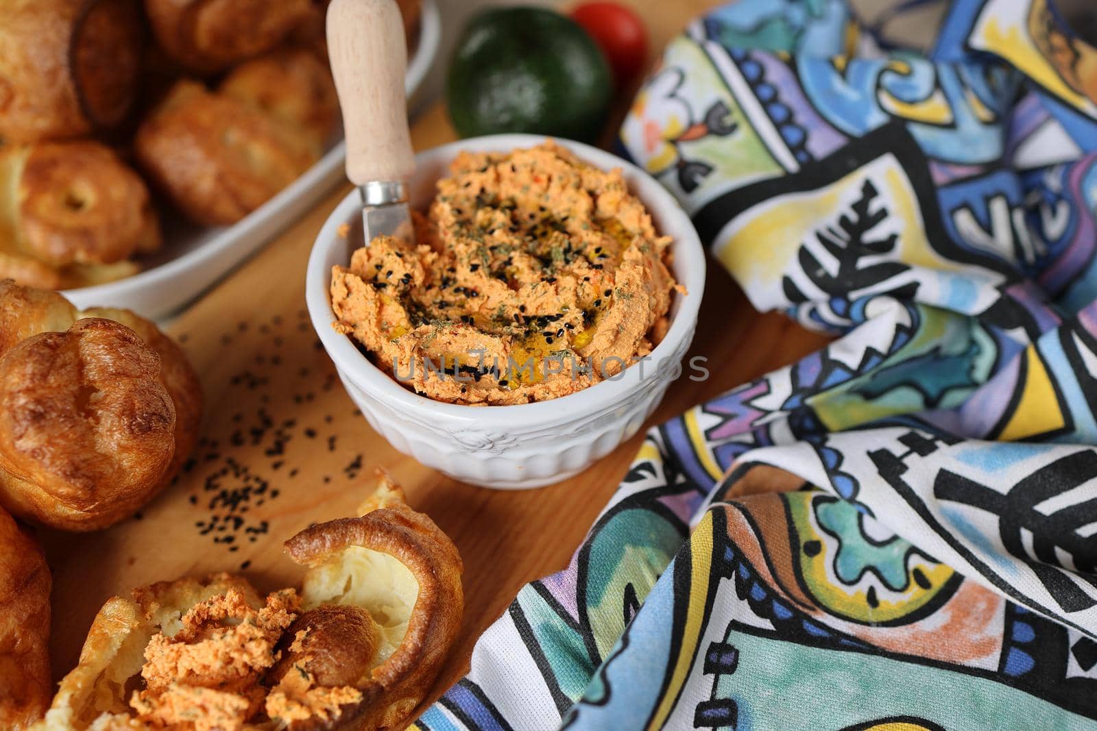 Homemade popover, which is a puffed, airy, and eggy hollow roll, is fresh from the oven and ricotta dip with sun-dried tomatoes and baked paprika in a ceramic white bowl