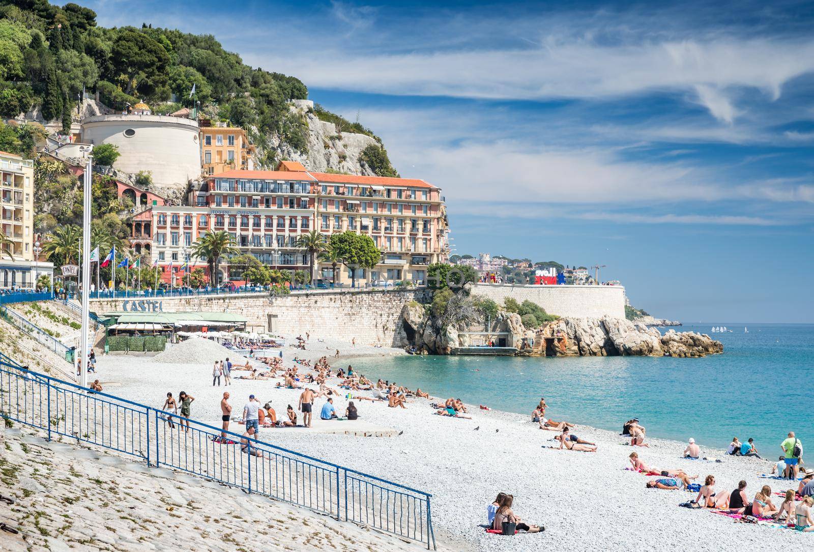 France, Nice, 15 May 2017: Promenade Anglais, Beautiful Public Beach, Tourists, Sunbath People, Swim, Sunny Day, People sit on the well-known blue chairs. High quality photo