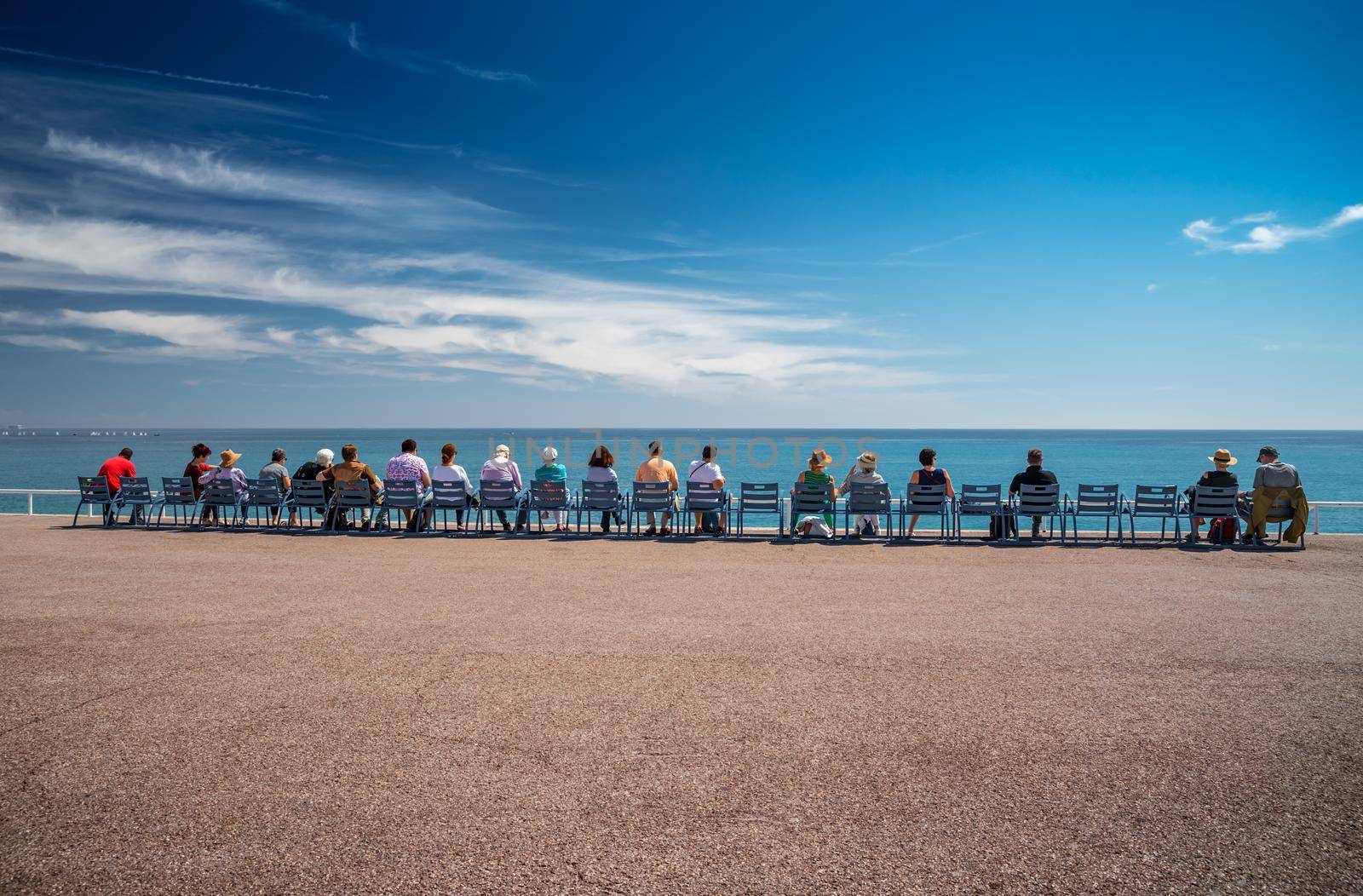 People sit on the famous blue chairs on embankment in Nice - France and watch at azure water of the Ligurian Sea, tranquillity, an old age, rest, age elderly people, the horizon, social. High quality photo