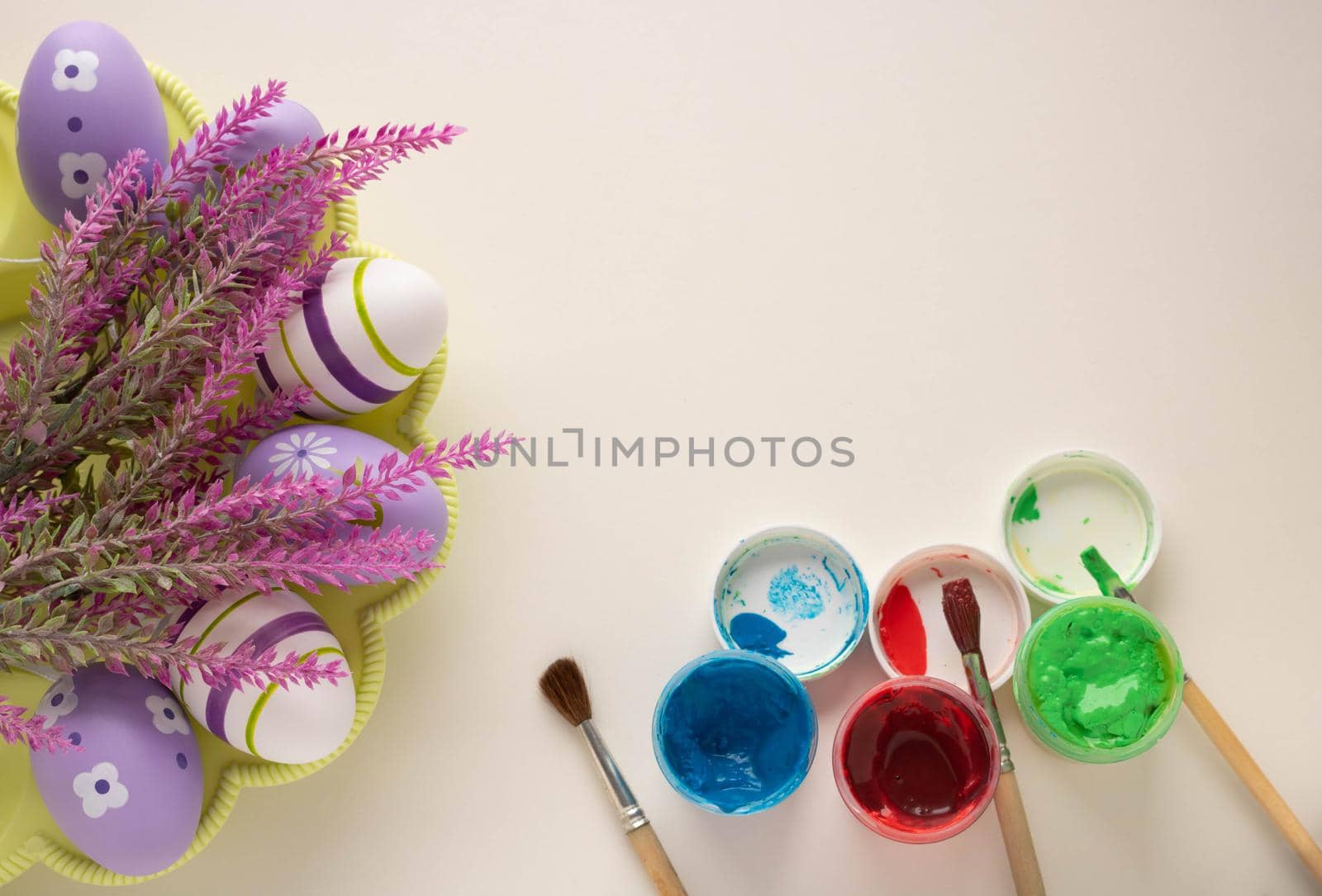 Brushes and open jars with gouache paint red, green, blue lie on a white background, prepared for coloring Easter eggs. Preparation for the Easter holiday.