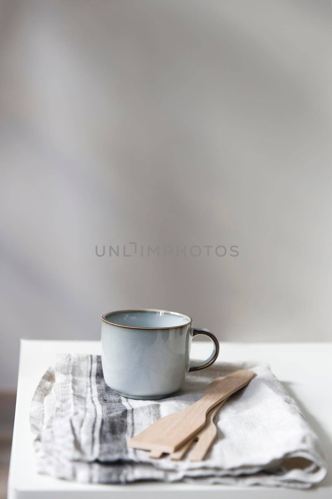 Two white mugs, a kitchen towel, a napkin and wooden frying utensils on the table. Defocus. by elenarostunova