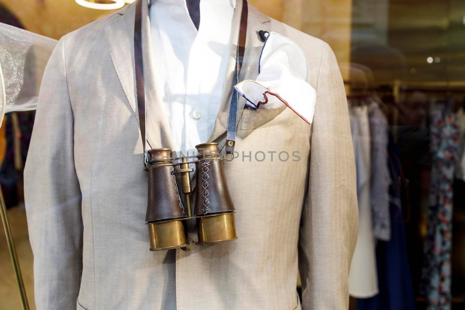 A fragment of a beige jacket and large vintage binoculars on the chest of a mannequin