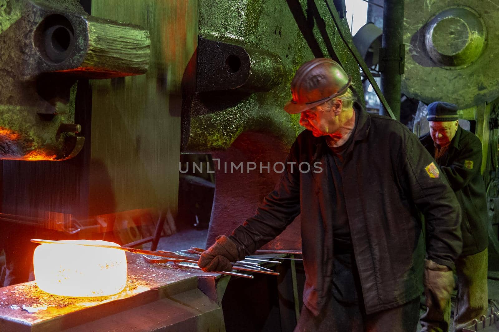 gray haired blacksmith worker forging large piece of hot steel in old factory with big steam hammer in Tula, Russia - February 1, 2020