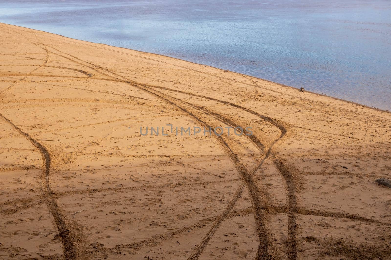 Tire tracks on the sand of an empty beach near the river.