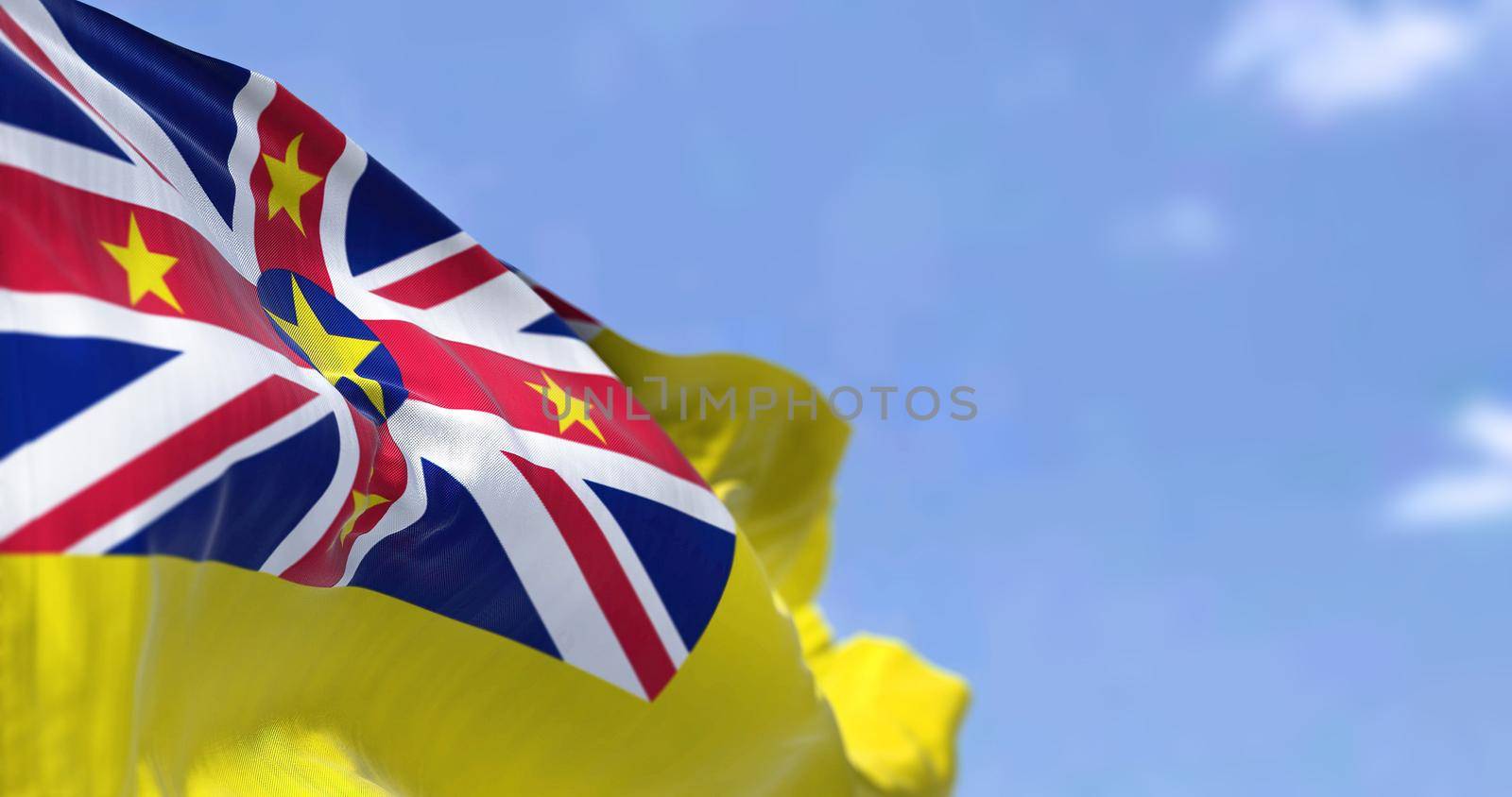 Close-up view of Niue state national flag waving in the wind. In the background there is a clear sky. Niue is an island state in the South Pacific Ocean. Selective focus