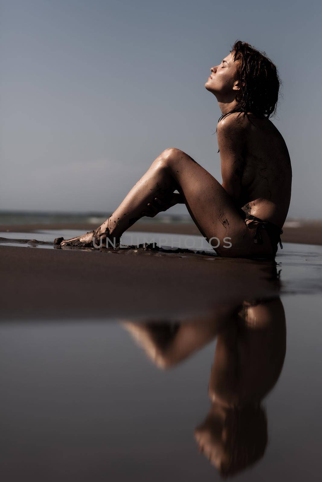 Sexy female body covered with sand. Girl on a beach with sea water reflection. . by kokimk