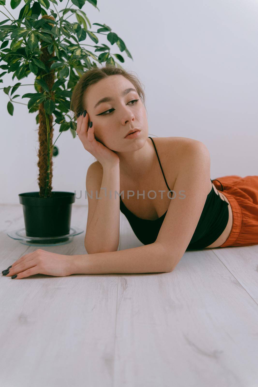 Portrait of young caucasian woman in red cloth laying near flowerpot. Dreamy