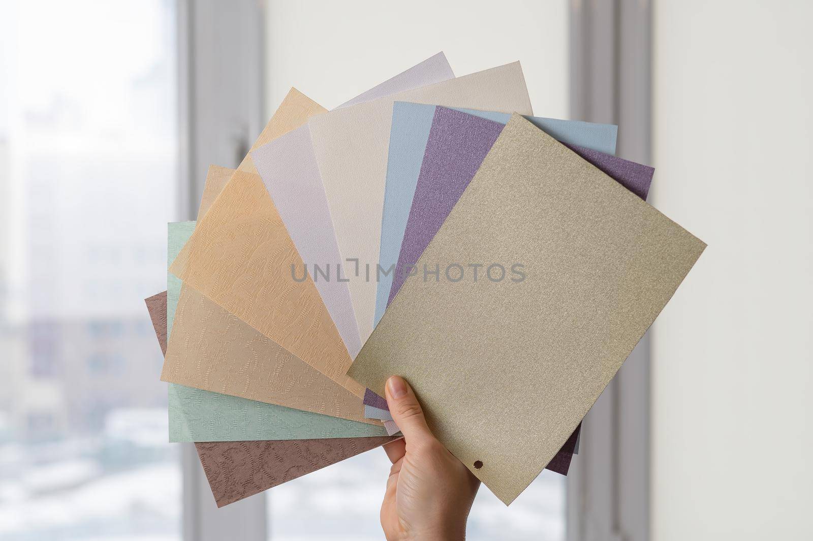 Woman holding fabric samples of roller blinds against window background