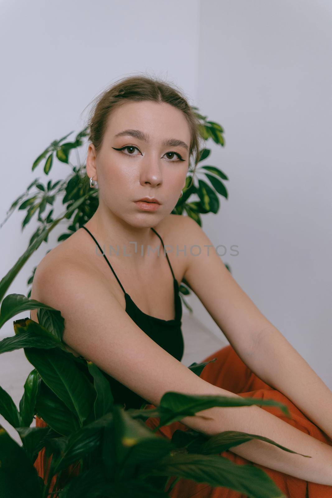 Portrait of young caucasian woman in red cloth sitting near flowerpot. Dreamy
