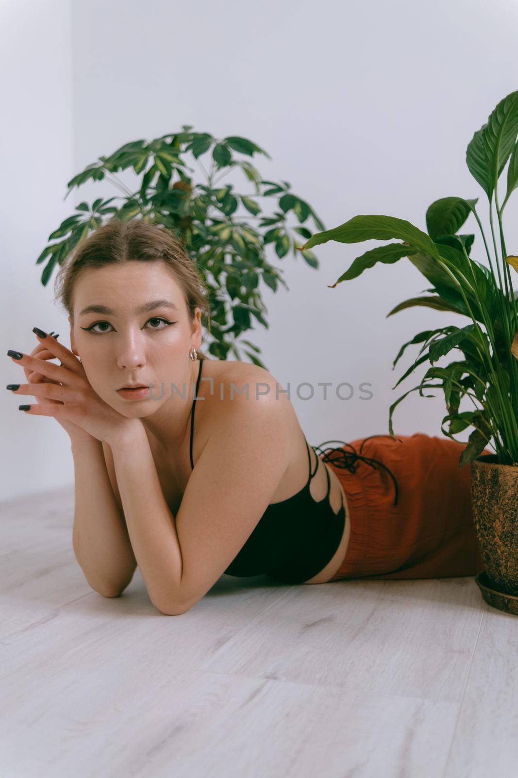 Portrait of young caucasian woman in red cloth laying near flowerpot by Symonenko