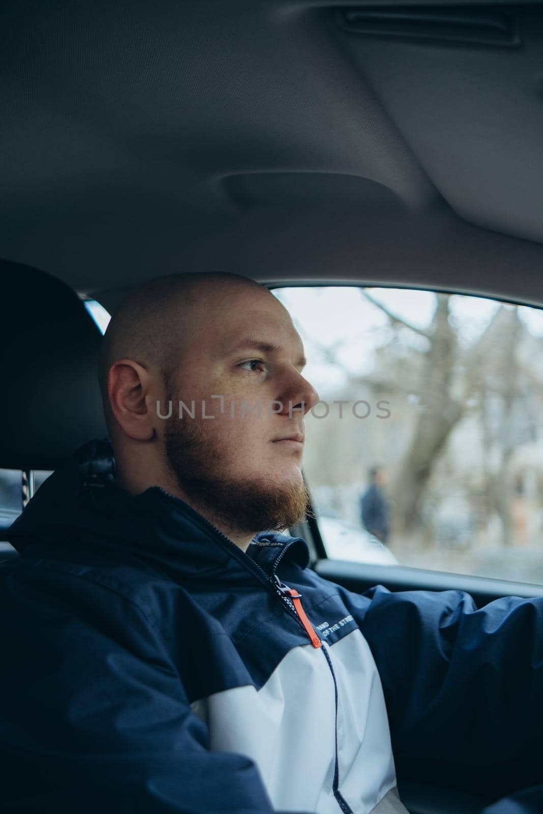 Handsome elegant bearded bald serious man drives a car by Symonenko