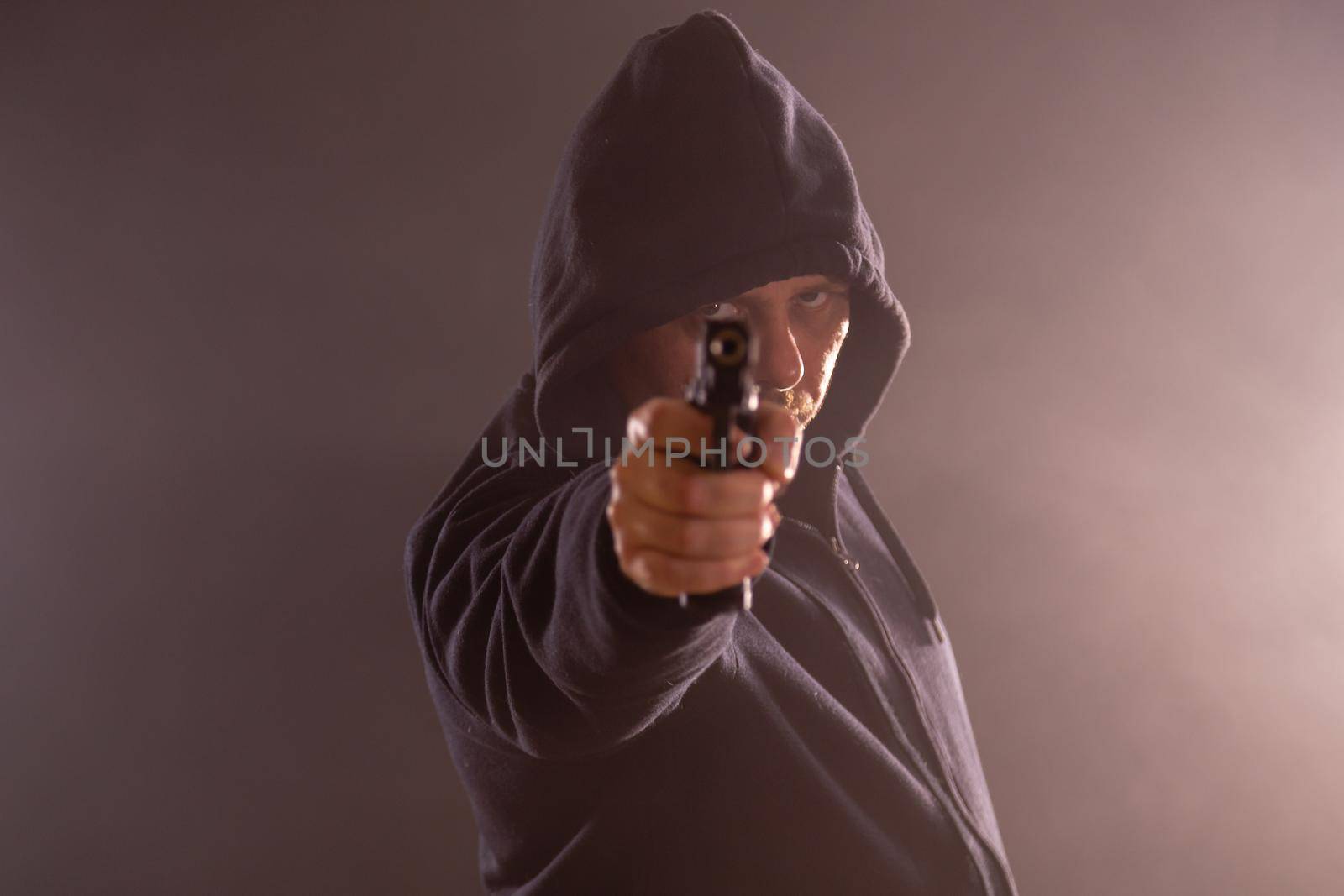 Man in black hoodie points handgun in smoke