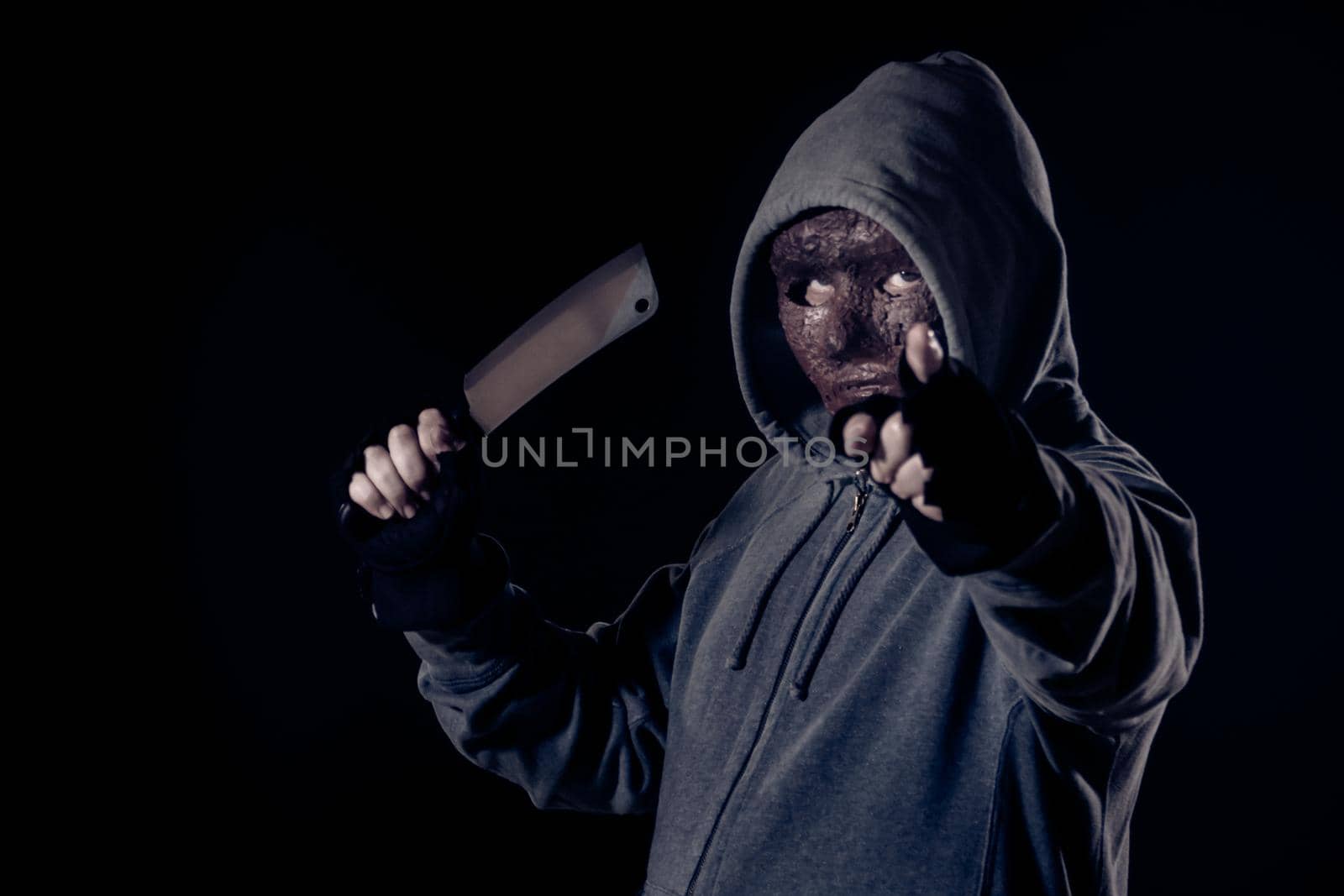 Scary killer in mask and hoodie holding knife and pointing finger