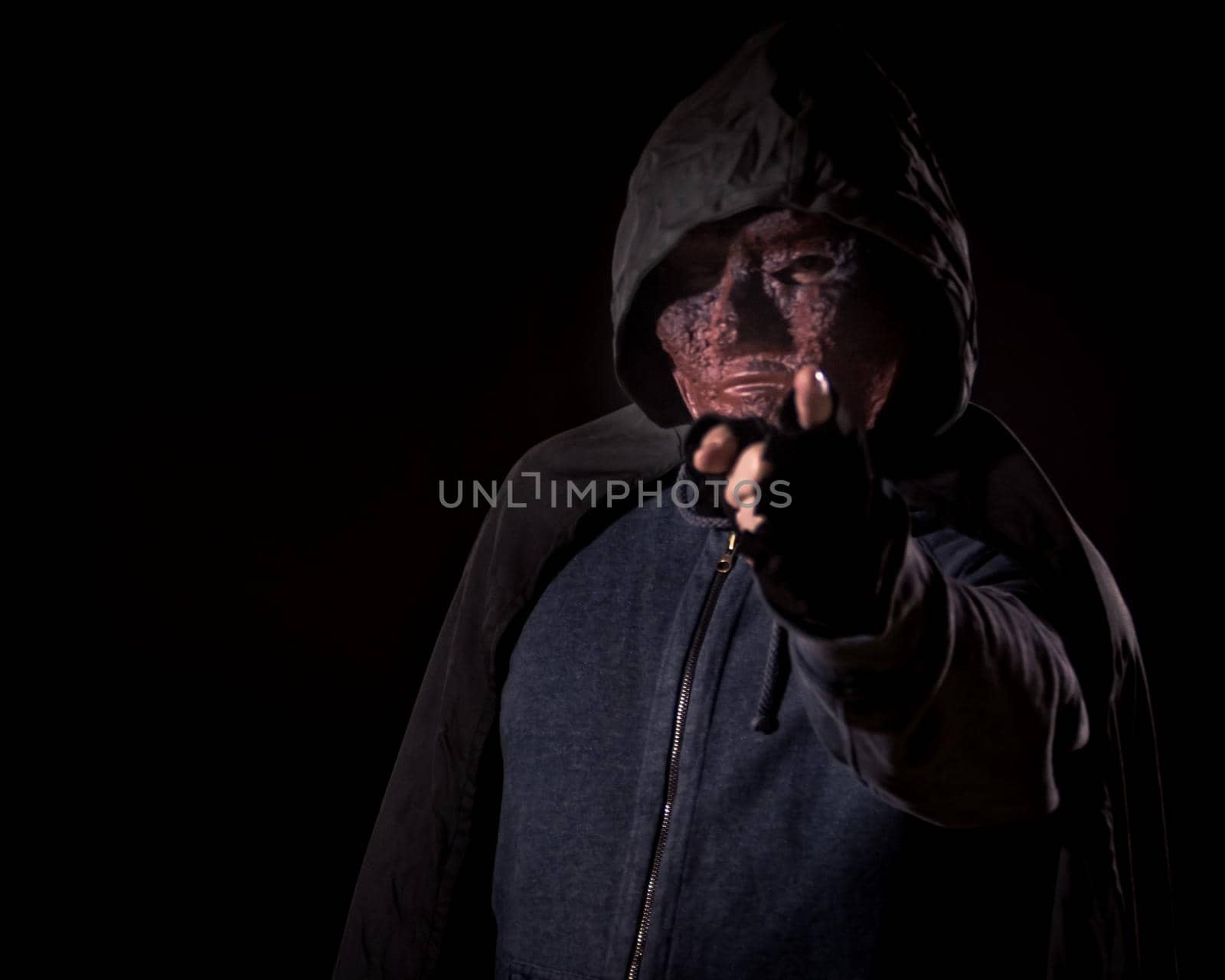 Scary killer in mask and hoodie pointing finger