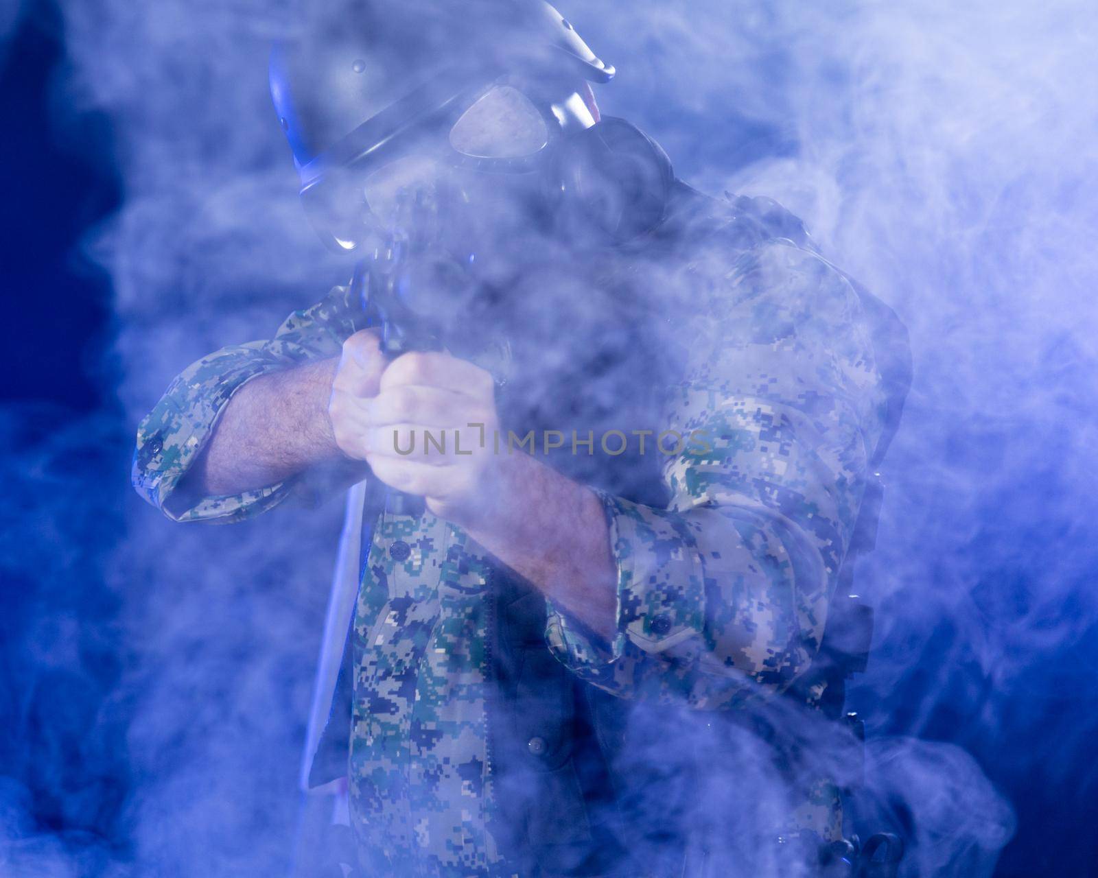 Soldier in army fatigues wearing gas mask holding assault rifle in haze of blue smoke