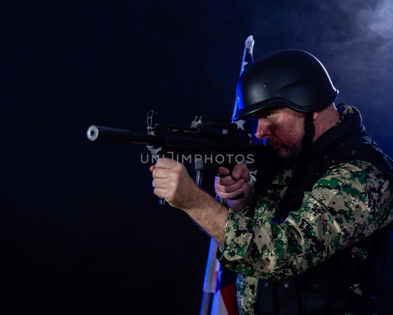 Soldier in army fatigues holding assault rifle in haze of blue smoke