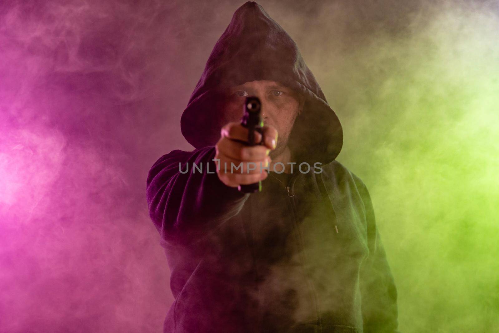 Man in black hoodie points handgun in colored haze of smoke