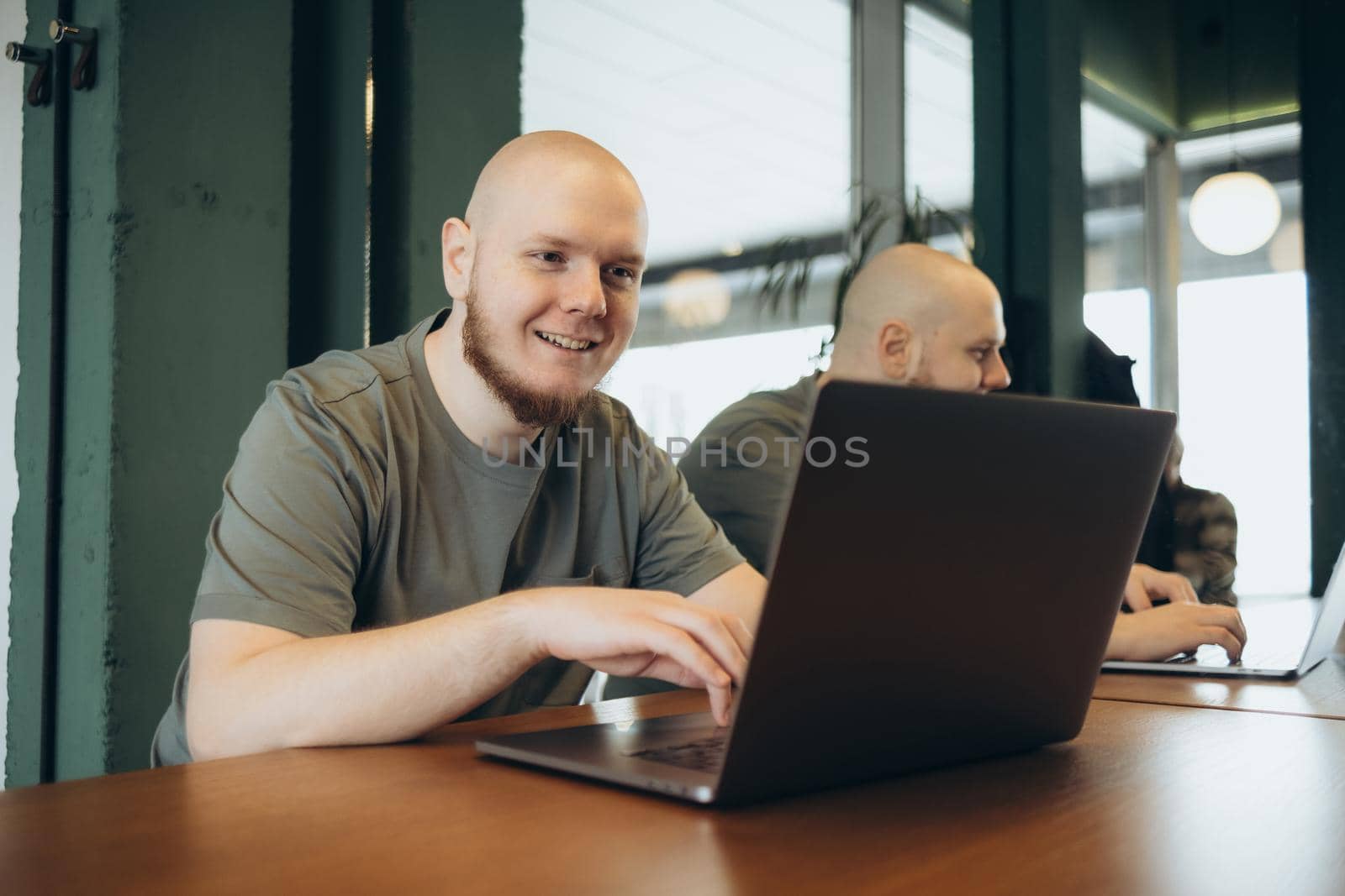 Unshaven happy man smiling and using laptop while sitting in cafe