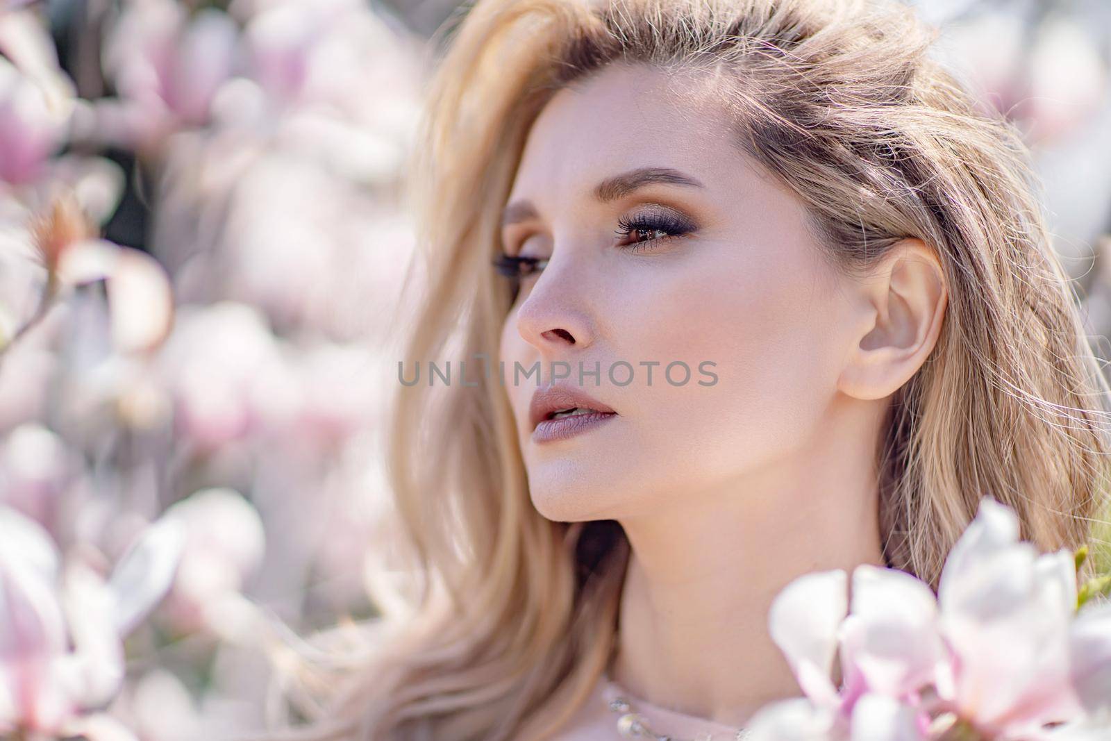 Portrait of a beautiful happy middle aged woman enjoying the smell in a blooming spring garden. Beautiful magnolia bushes, large flowers