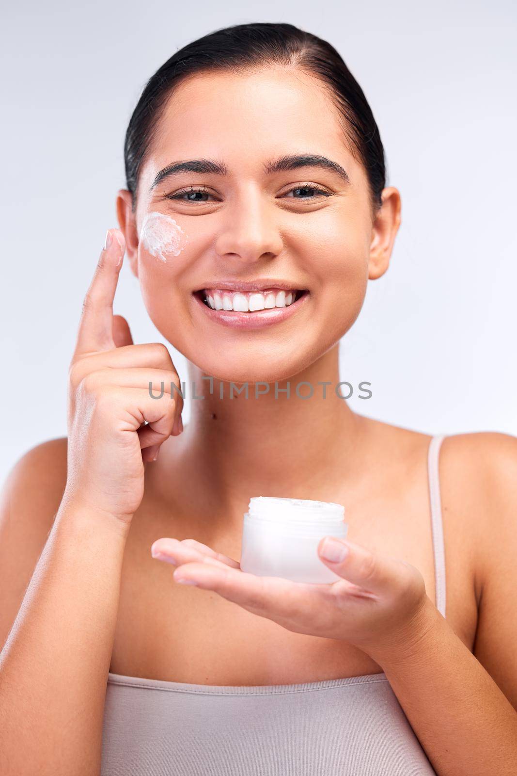 This moisturiser leaves my skin hydrated and smooth. Shot of a beautiful young woman applying moisturiser to her face. by YuriArcurs