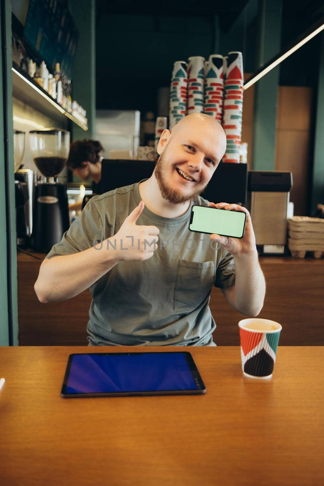 Cheerful male pointed at empty blue screen of tablet by finger while sitting on bench near modern cafe and looking at camera