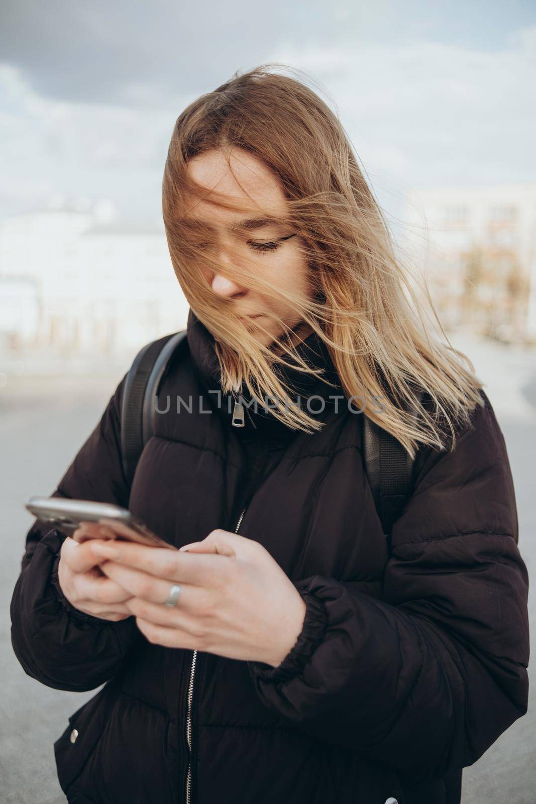 gorgeous beautiful young woman with blonde hair messaging on the smart-phone at the city street background. by Symonenko