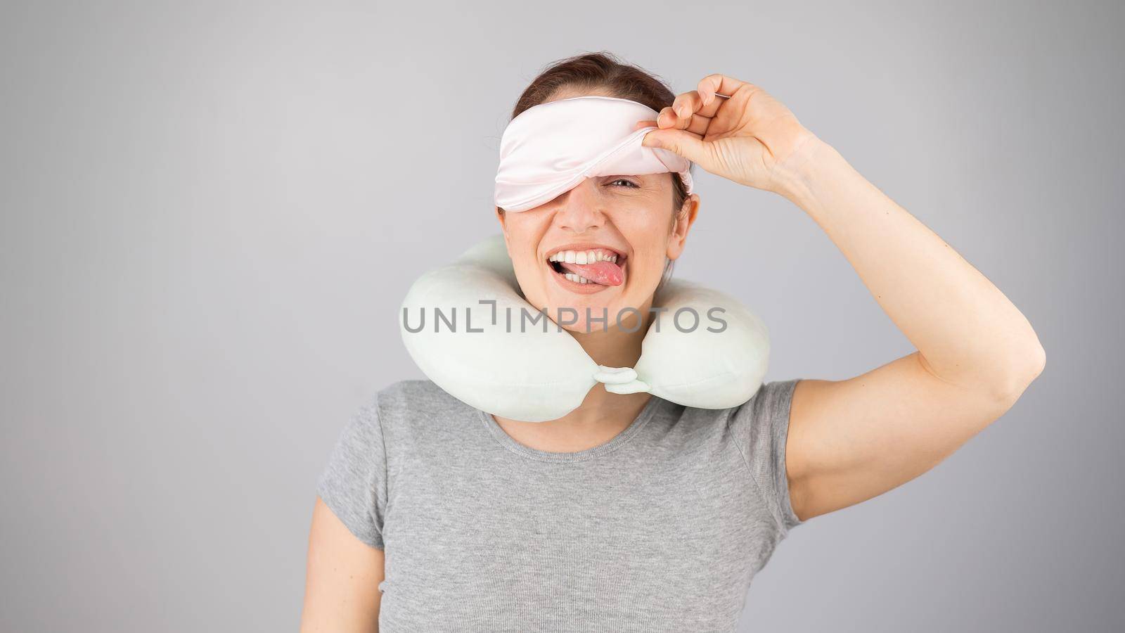 Smiling caucasian woman with a travel pillow takes off her sleep mask on a white background