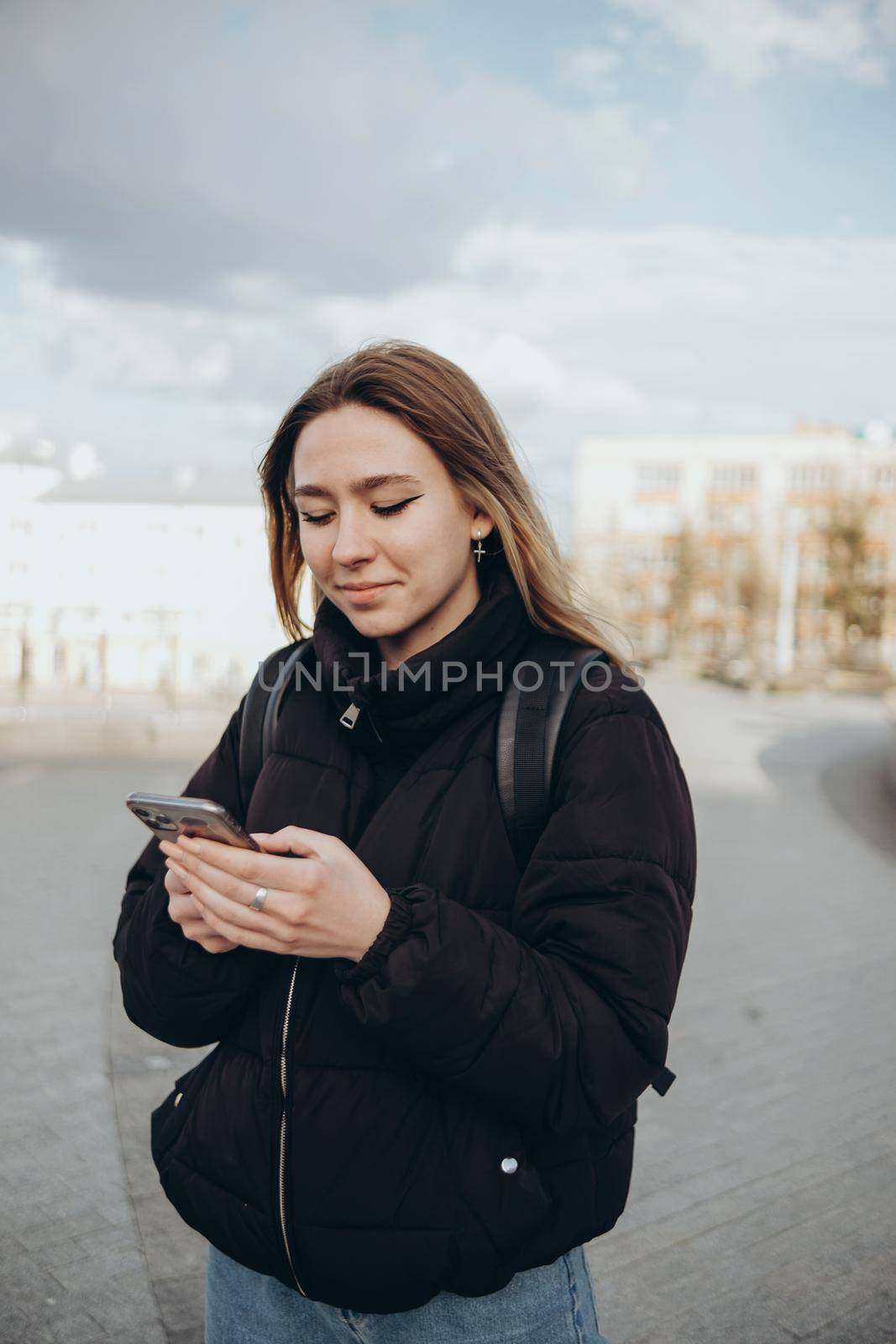 gorgeous beautiful young woman with blonde hair messaging on the smart-phone at the city street background. by Symonenko