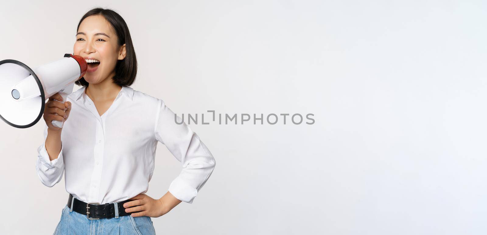 Image of young woman, korean activist, recruiter screaming in megaphone, searching, shouting at loudspeaker, standing over white background by Benzoix