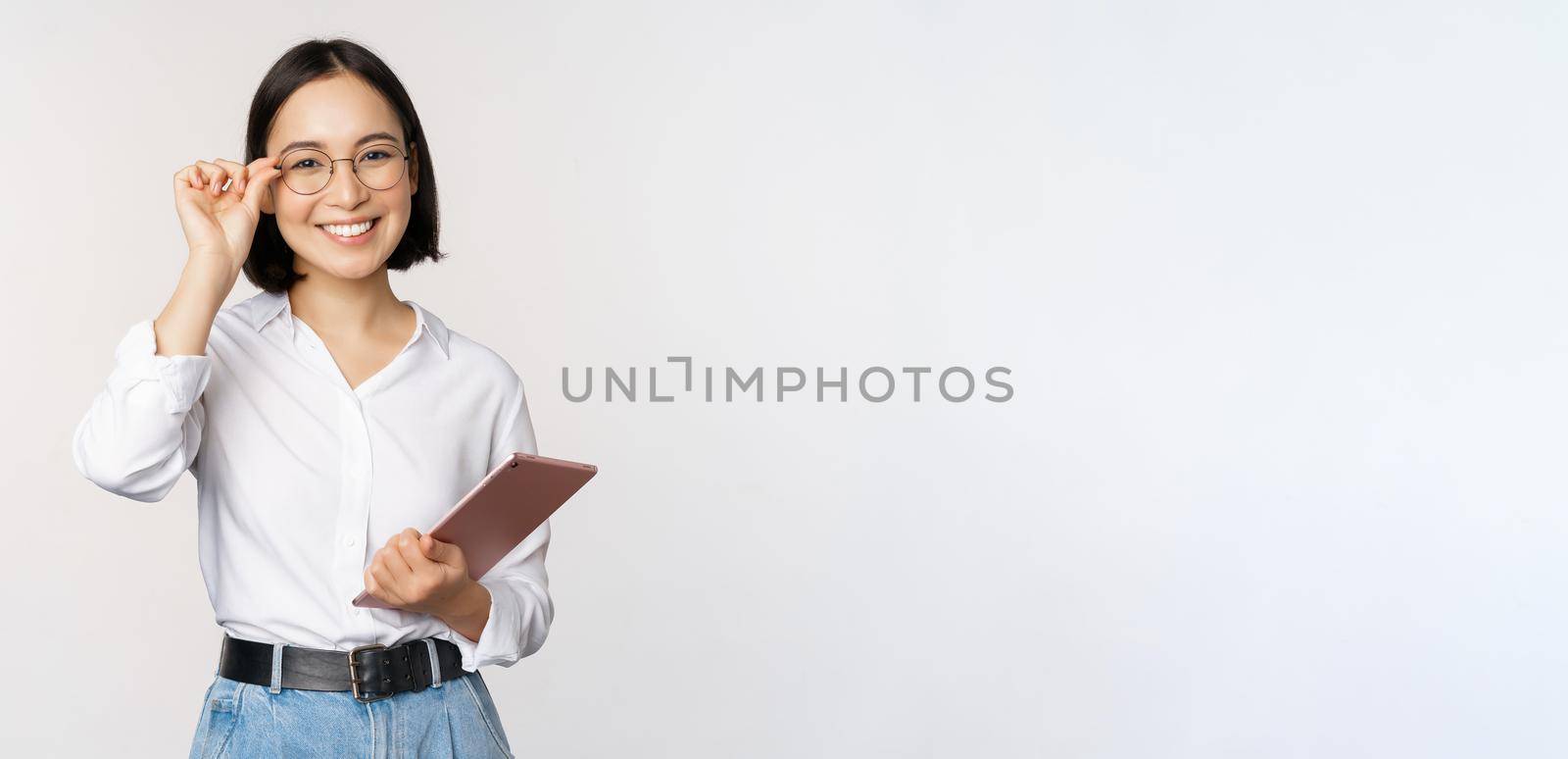 Image of young asian business woman, female entrepreneur in glasses, holding tablet and looking professional in glasses, white background by Benzoix