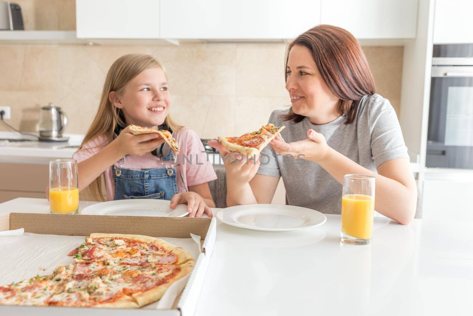 Mother and daughter sitting in the kitchen, eating pizza and having fun. Focus on the daughter