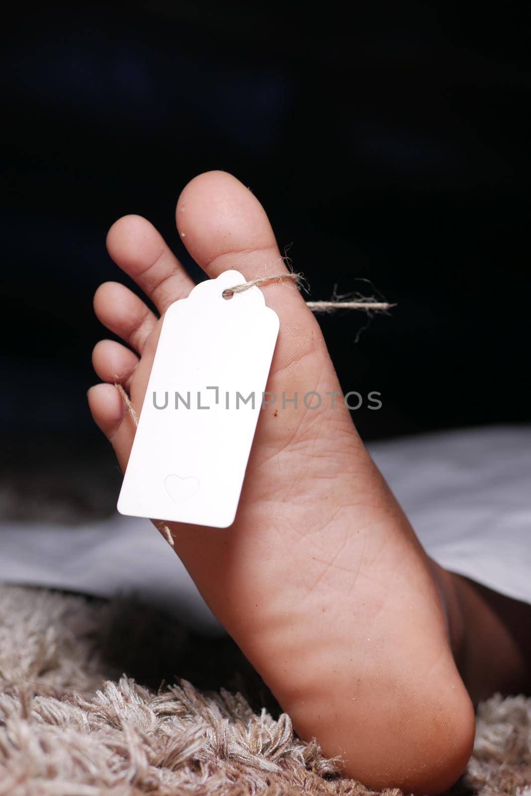 The dead man's body with tag on feet under white cloth in a morgue.