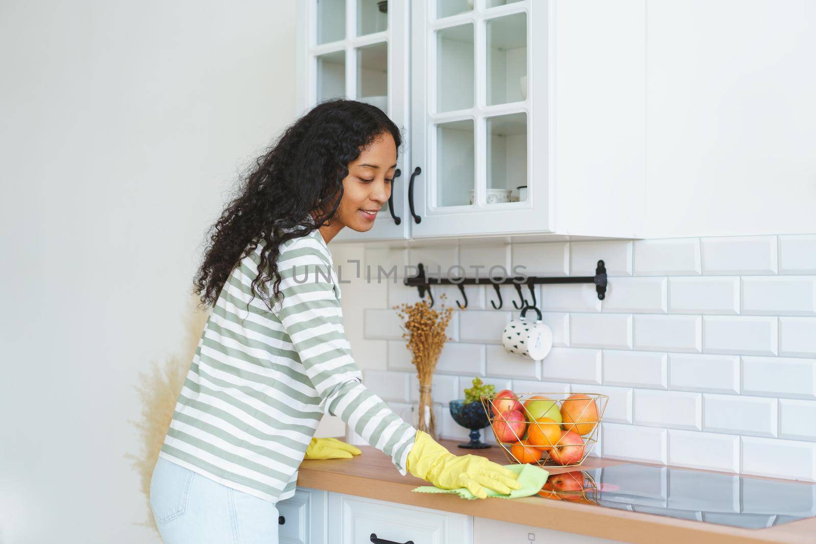 African-American female dust handling kitchen with washcloth. Concept of cleaning modern kitchen and doing household chores. Removing dirt from kitchenette unit after finishing cooking