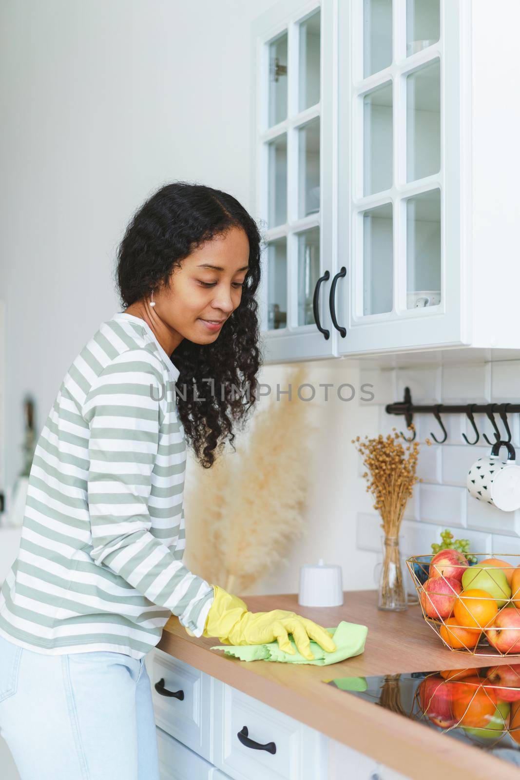 African-American woman in rubber gloves sweeping and cleaning stove with washcloth. Concept of doing household chores and removing dirt from modern kitchen surface