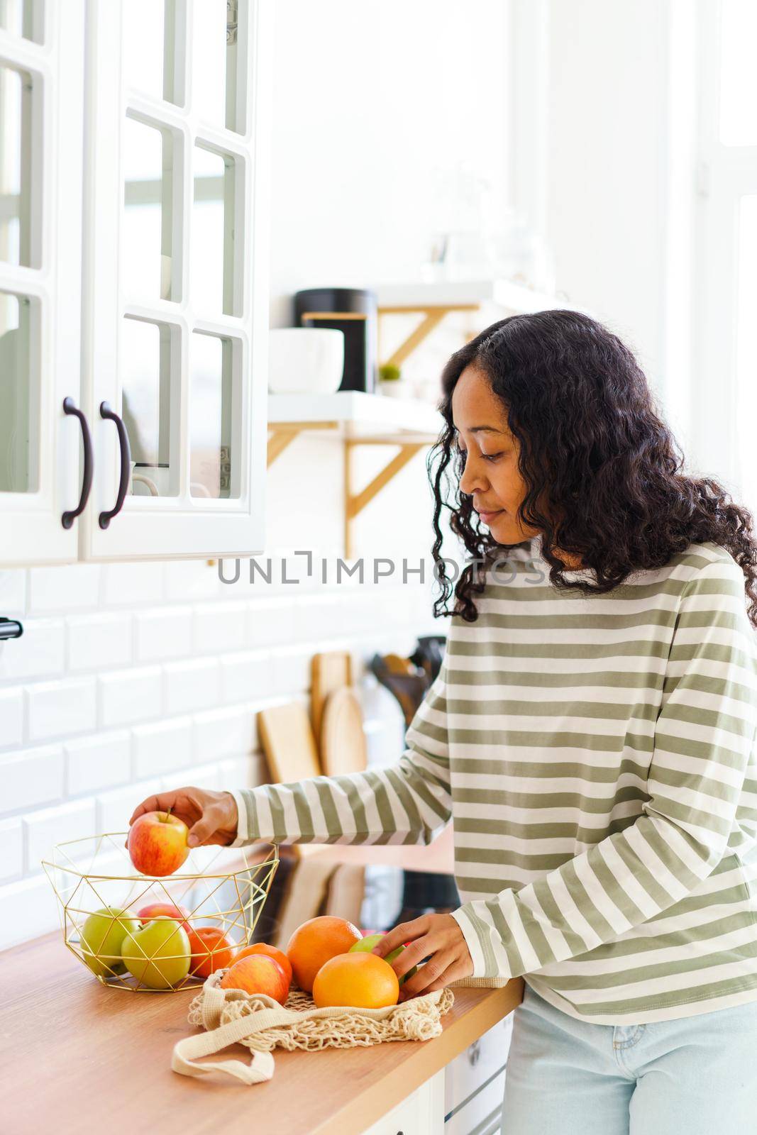 African-American woman sorting green and red apples with oranges after shopping in grocery store. Concept of healthy vegan products. Dietary fruits and citrus. Sweet nutritious snack
