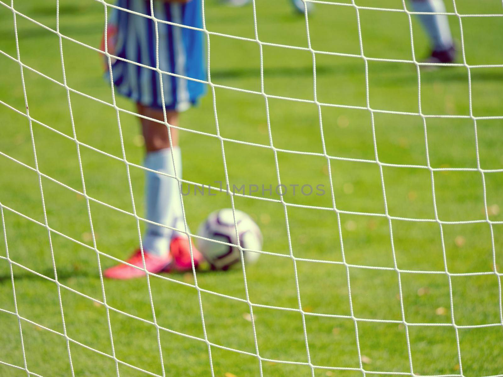 Young football goalkeeper in fotball field. Out of focus. View through the football gate net. 