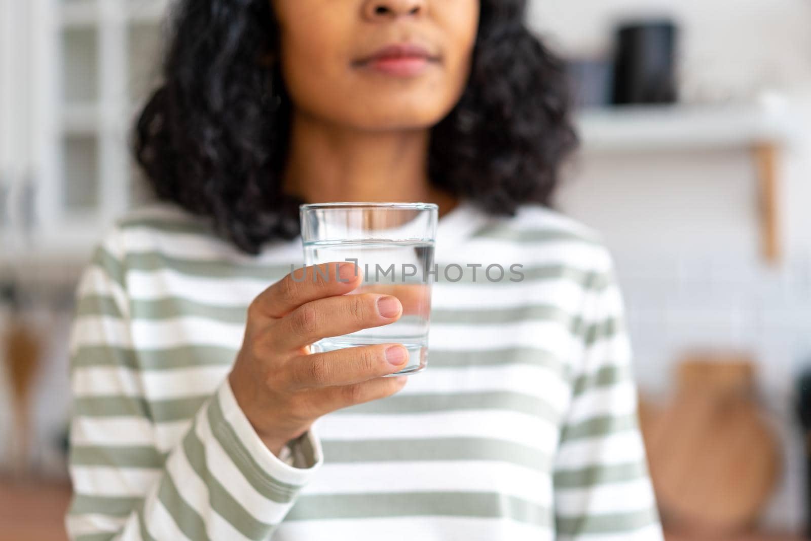 Cropped anonymous african-american woman taking sip of water. Healthy and refreshing start of day. Concept of thirst and relish. Faceless in comfy clothes. Selective focus, horizontal