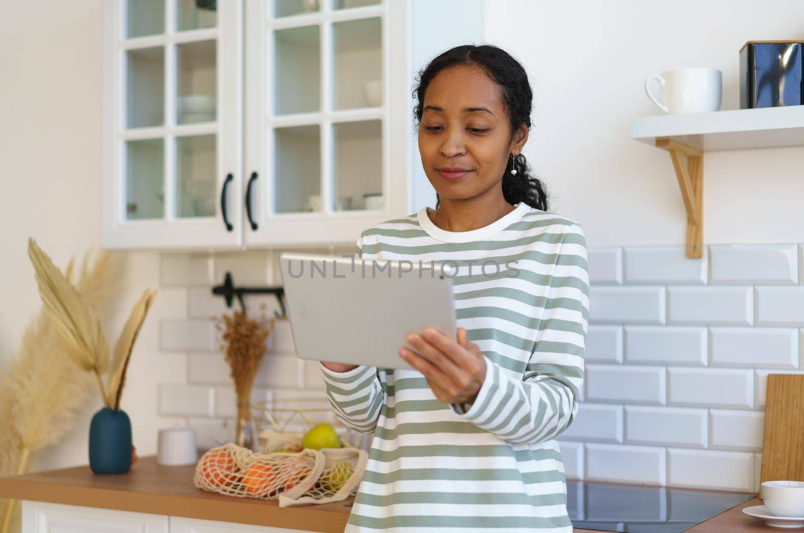 African-american woman using pad in kitchen. Looking for apple recipe before cooking. Surfing the net online. Concept of modern clever female watching films on digital device. Horizontal, copy space