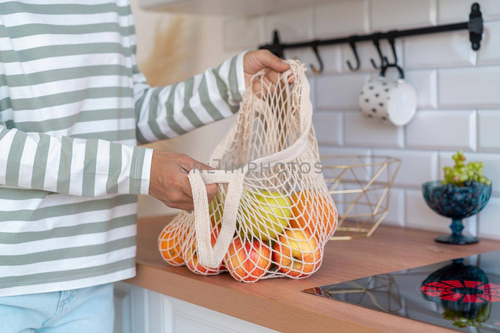 Faceless female buying fruits in eco bag. Sorting green and red apples, oranges in kitchen. Eco-friendly shopping concept. Vegetarian healthy products. Sustainable alternative. Plastic free package
