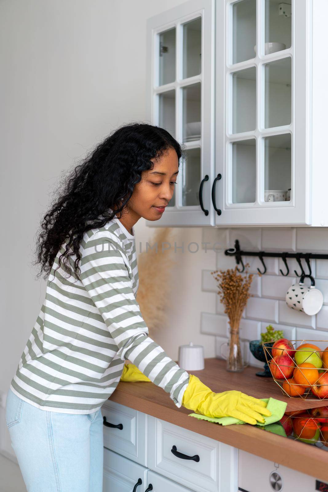 African-american woman occupied with household duties in kitchen. Wearing yellow rubber gloves by NataBene