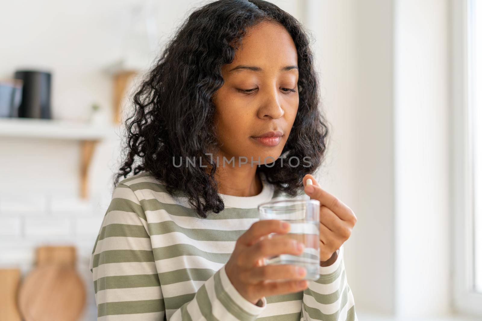 African-american woman taking medicine with glass of clear water. Healthy treatment at home. Concept of recovering from illness while washing down drugs. Vitamins for health issues